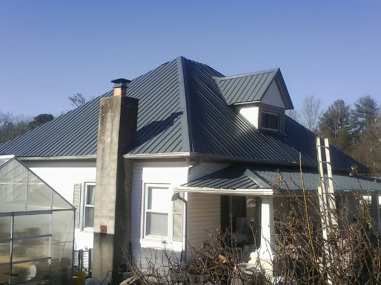 Dark blue standing seam metal roof on a white farmhouse with dormer — Slate & Tile Roof Repair by Roofing Brothers in Donora
