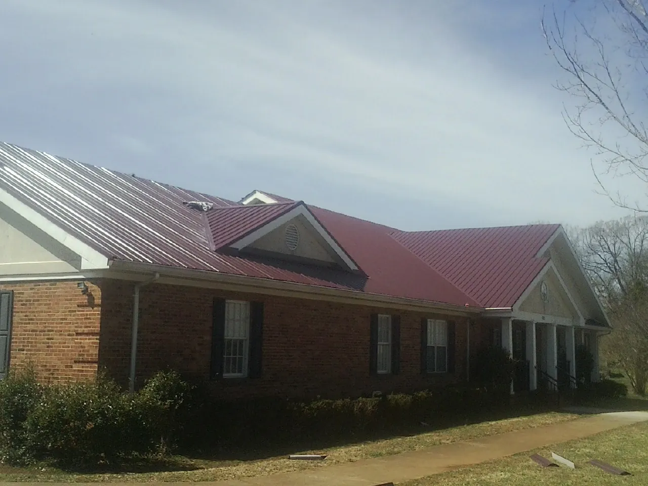 Red metal roof with gabled entries on a long brick building, from a Hail Damage Roof Repair job in Donora