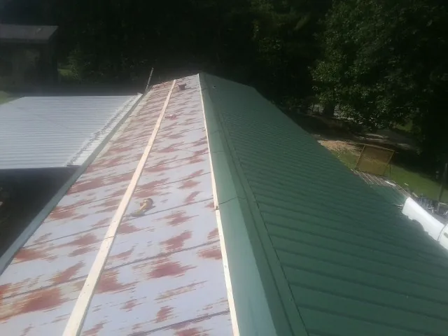 Old rusted panels beside newly installed green metal roofing — Wind Damage Roof Repair by Roofing Brothers in Donora
