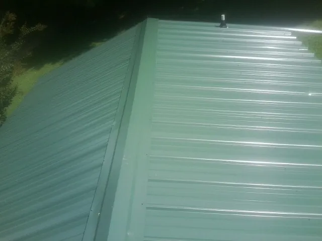 New green metal panels meeting at the ridge of a roof — Flat Roof Repair work by our crew in Donora