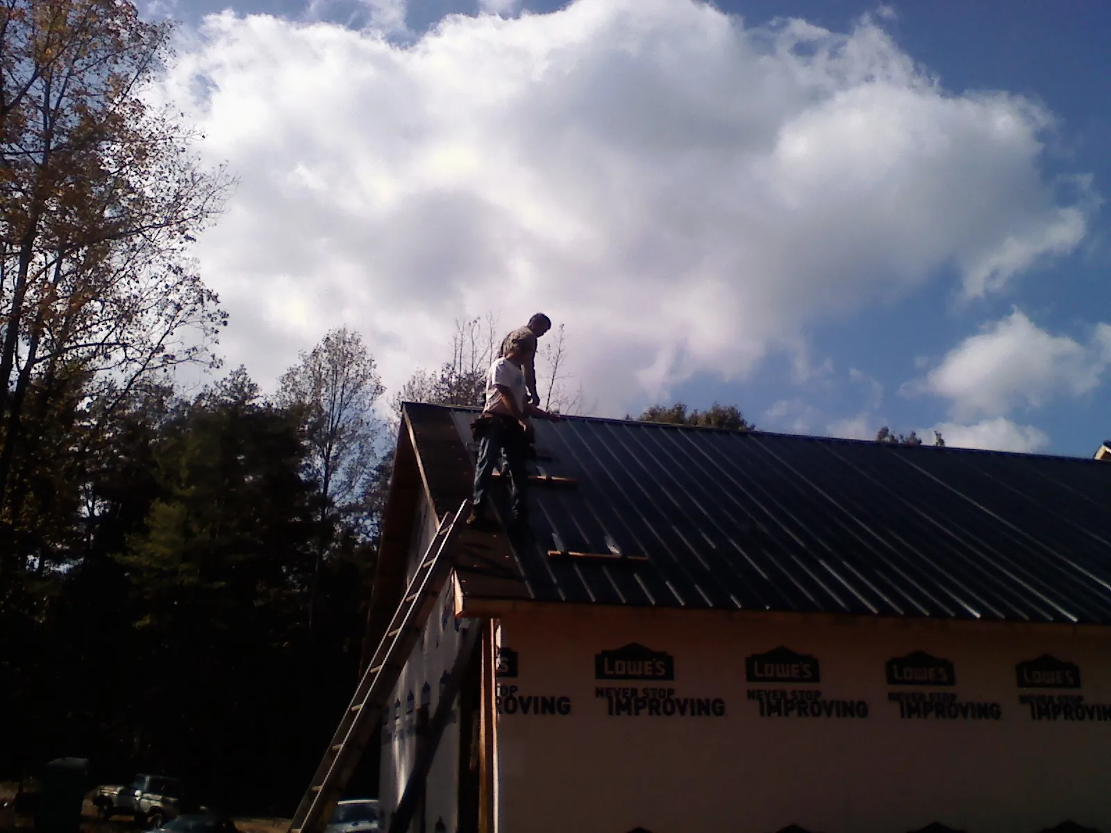 Roofer fastening dark metal panels high against a cloudy sky, from a Roof Inspection job in Donora