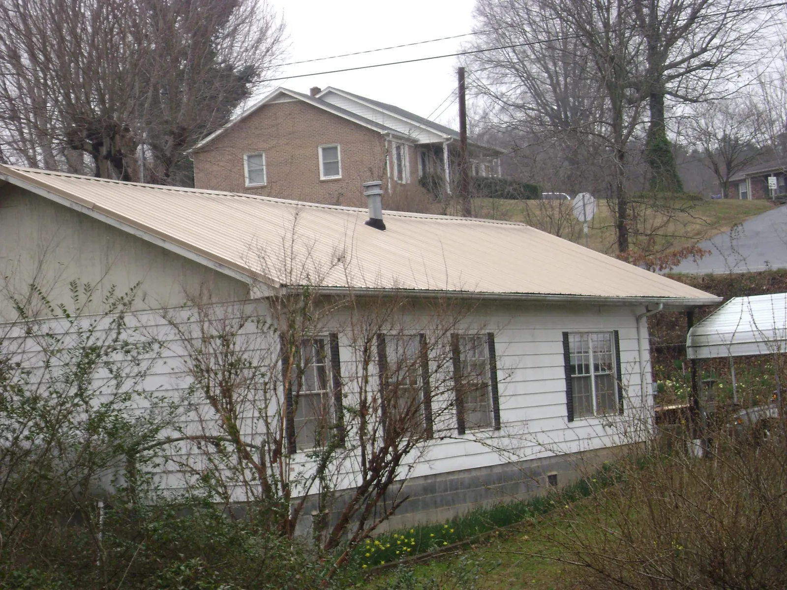 Tan metal roof on a white sided house set into a hillside — Commercial Roofing by Roofing Brothers in Donora