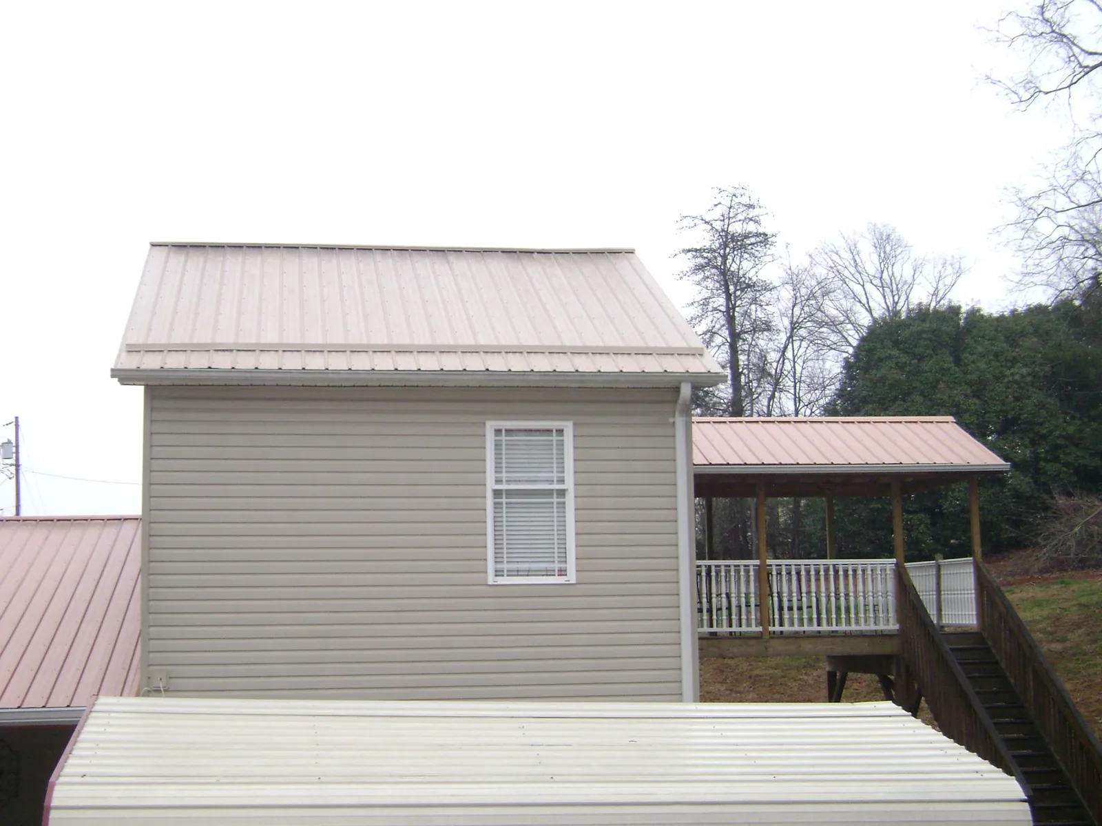 Tan metal roofs on a two story addition and attached porch, from a Roof Replacement job in Donora